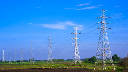 Perspective and side view of high voltage towers with cable lines in countryside in blue sky...