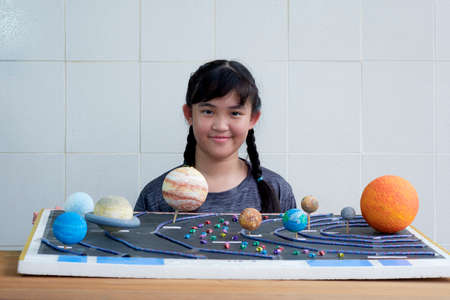 Young smiling Asian girl showing her homemade solar system model for science homework project at schoolの写真素材