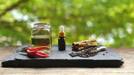 Dropper bottle with herbal essential oil in glass jar and various herbs on black stone plate and wooden table floor in blurred greenery backgroundの写真素材