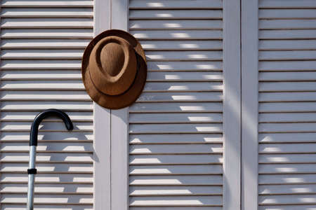 Sunlight and shadow on surface of fedora hat with metal walking stick on white wooden folding wall background in vintage tone styleの写真素材