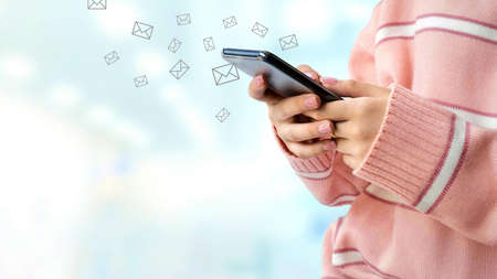 Close up young female hand in pink sweater using smartphone sending emails  with blurred interior lighting in blue area backgroundの写真素材