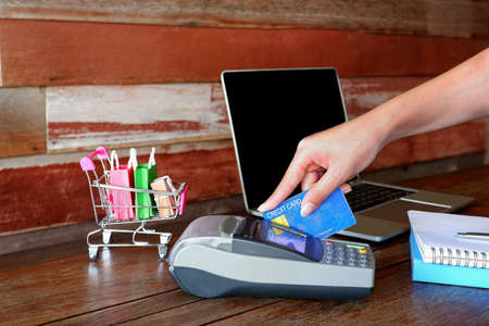 Female hand using credit card swipe through payment terminal for buy products with laptop, small...