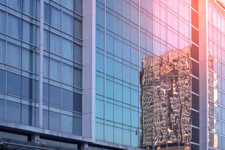 Low angle and side view of blue glass wall with reflection pattern of skyscraper and flare light on surface, architecture and buildings exterior design conceptの写真素材