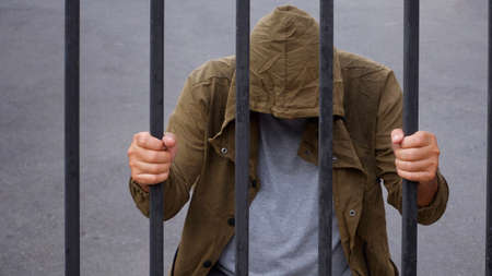 Despair man in hood bend down the head and holding iron bars, immigrant and refugee crisis in...