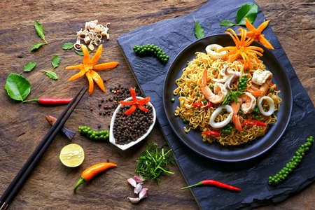 Flat lay of instant noodles with stir fried spicy seafood and various spices on black stone plate with wood background, junk food and Asian meal  conceptの写真素材