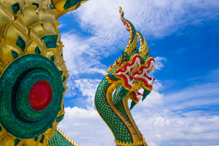 Low angle and side view of colorful 3-headed serpent statue against white cloud in blue sky backgroundの写真素材