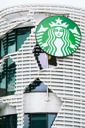 Samut Sakhon, Thailand - November 21,2020 : Large glowing Starbucks logo sign on futuristic geometric pattern of the old white exterior building on cloudy day in vertical frameのeditorial素材
