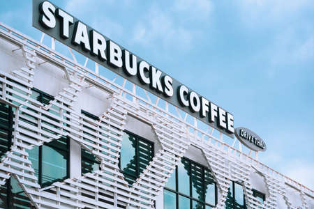Samut Sakhon, Thailand - November 21,2020 : Low angle and side view of Starbucks coffee drive thru label on top of the old white building in modern style against cloud with blue skyのeditorial素材
