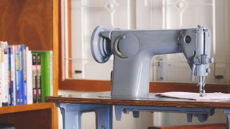 The old gray sewing machine with blurred bookshelf in living room background for vintage home interior decoration conceptの写真素材