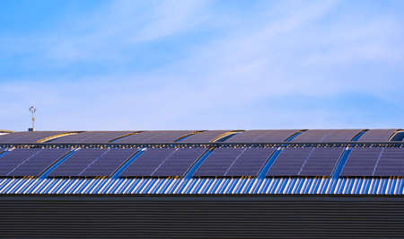 Many solar panels on curved steel roof of industrial building against blue sky backgroundの写真素材