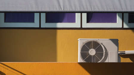Sunlight and shadow on surface of air conditioning compressor with row of glass windows and roller canvas blind on balcony of the old yellow house building in vintage tone styleの写真素材