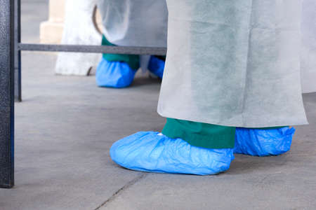 Low section of 2 health workers in PPE clothing wore blue protective plastic bags on feetの写真素材