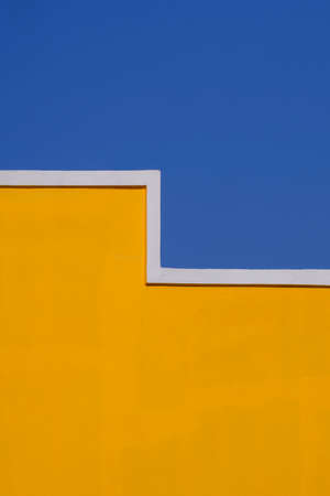 Geometric pattern of empty yellow cement building wall against blue clear sky in vertical frame for...