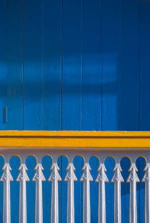 Sunlight and shadow on surface of white balustrade on terrace in front of blue wooden door in...