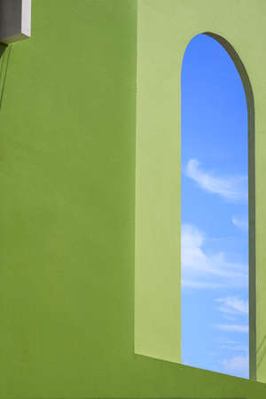 Perspective side view of blue sky inside of open exterior window arch frame on green concrete wall...