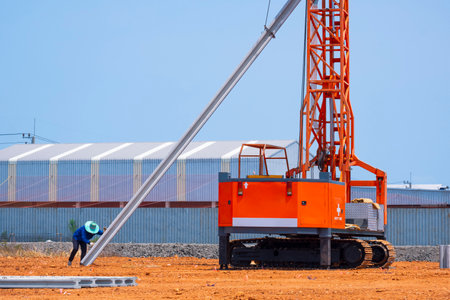 Construction worker with crawler pile driver machine lifting concrete piling for install industrial...