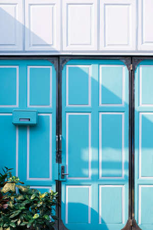 Sunlight and shadow on surface of mailbox on entrance door of vintage blue and white wooden house with green house plant in vertical frameの写真素材