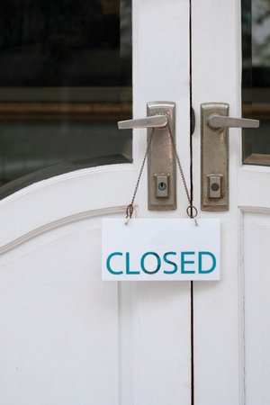 Front view of closed sign label hanging on door handle of the old white vintage door in vertical frameの写真素材