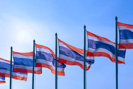 Row of many Thai flags on flagpoles waving in the wind against blue clear sky in sunny dayの写真素材