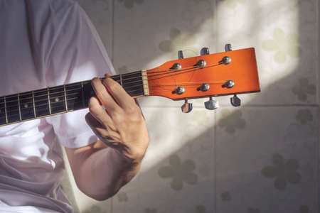 Sunlight and shadow on surface of teenage boy hand practicing to play the guitar at home
