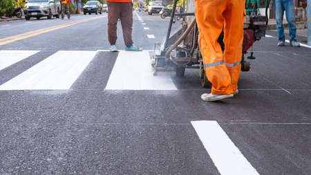 Low section of road workers group with thermoplastic spray marking machine are painting pedestrian crosswalk on asphalt road in the cityの写真素材