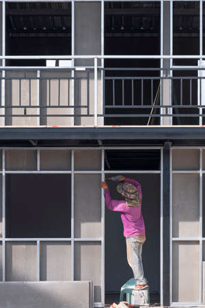 Front view of Asian construction worker installing precast concrete wall inside of house construction siteの写真素材