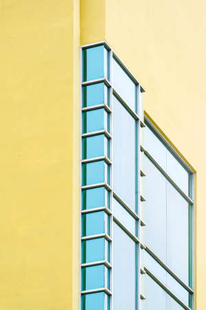 Geometric pattern of blue glass wall on modern yellow building in vertical frame, low angle and perspective side viewの写真素材
