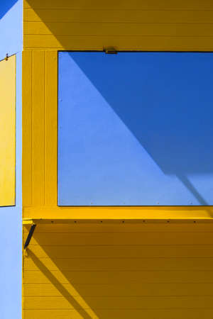 Sunlight and shadow on surface of yellow and blue coffee street kiosk in vertical frame