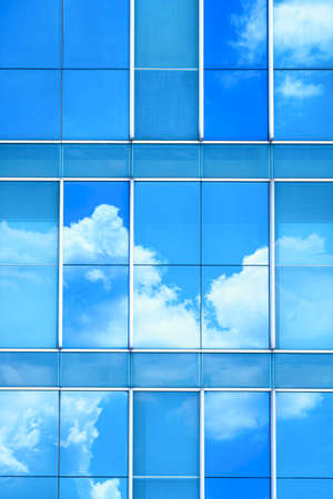Cloud and blue sky reflection on surface of glass modern building wall in vertical frameの写真素材