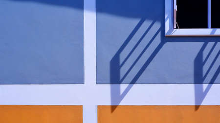 Sunlight and shadow on surface of white wooden window with blue and orange painted wall decoration background, exterior architecture conceptの写真素材