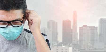 Close up Asian man in eyeglasses with gray t-shirt wearing protective mask and blurred dusty city...