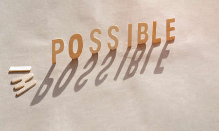 Sunlight and shadow on surface of falling "I" and "M" wood alphabets with POSSIBLE word stand on paper board, Concept for chance impossible to possible by attitude changeの写真素材