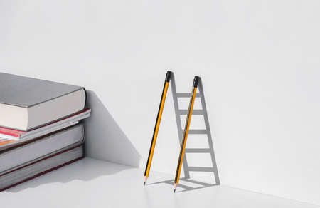 Two pencils and shadow in form of ladder with stack of textbooks on white tabletop, Education, learning is the ladder to success conceptの写真素材