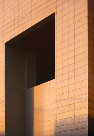 Morning sunshine on surface of geometric apertures window on gray tile wall of modern office building in perspective side viewの写真素材