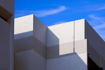 Sunlight and shadow on surface of white building against blue sky backgroundの写真素材