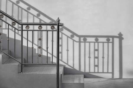 Stainless steel handrail of vintage outdoor staircase with sunlight and shadow on cement wall in black and white styleの写真素材