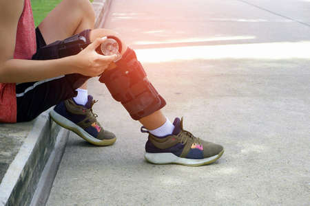 Part of teenager boy sitting and turns angle movement control of supportive knee brace on his leg...