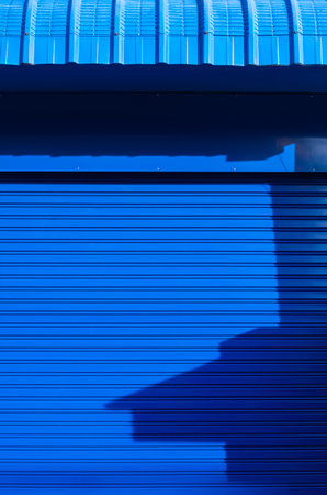 Sunlight and shadow on surface of automatic blue roller shutter door with steel awning in vertical frameの写真素材