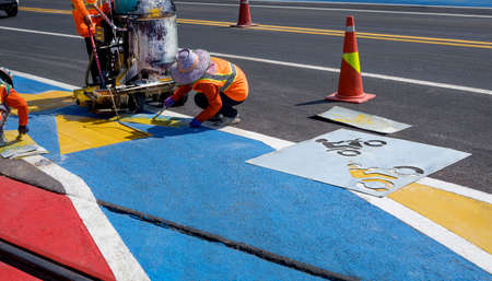 Road workers group with thermoplastic spray road marking machine are working to paint traffic sign...