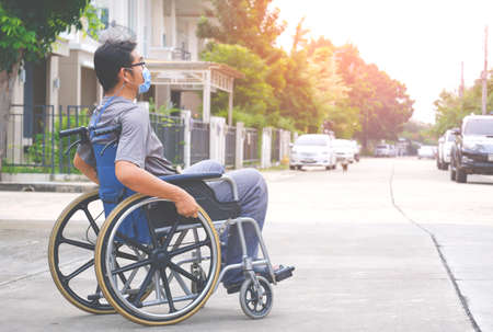 Side view of Asian disabled man wears protective mask on wheelchair crossing the street in housing estateの写真素材