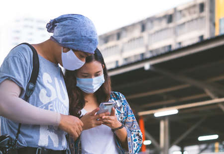 Young Asian hipster couple in protective mask using smartphone to checking destinations while traveling by trainの写真素材