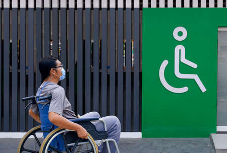 Asian adult man on wheelchair with protective mask is going to public restroom adapted for disabled person at gas stationの写真素材