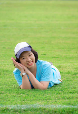 Portrait of Asian plus size woman lying down on grass field and smiling comfortably for the camera after exercise in public parkの写真素材