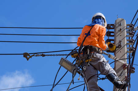 Low angle view of electrician with safety equipment and various work tools is installing cable lines...