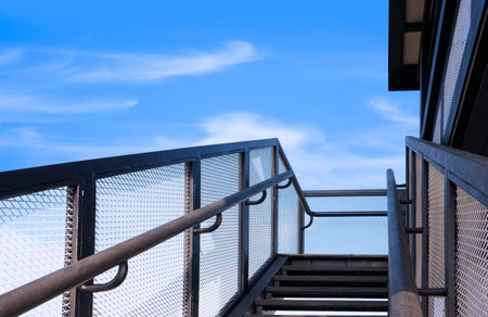 Low angle view of black metal staircase with handrail outside house against blue sky backgroundの写真素材
