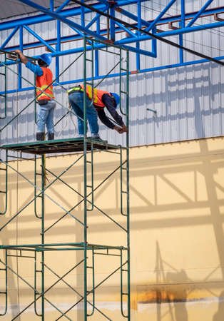Two construction workers are installing high scaffolding for construction of warehouse building structure in construction siteの写真素材