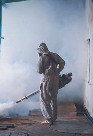 Rear view of outdoor healthcare worker using fogging machine spraying chemical to eliminate mosquitoes and prevent dengue fever at slum area in vertical frameの写真素材