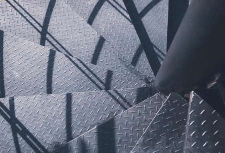 Top view of black metal steps of outside spiral staircase with sunlight and shadow on surface