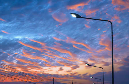 Silhouette row of street lampposts against colorful sunset sky background in low angle viewの写真素材