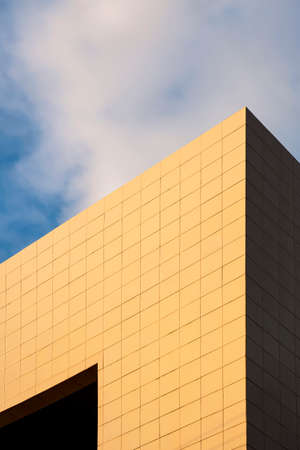 Golden sunlight on surface of modern office building wall against white clouds with blue sky at morning time in perspective view and vertical frameの写真素材